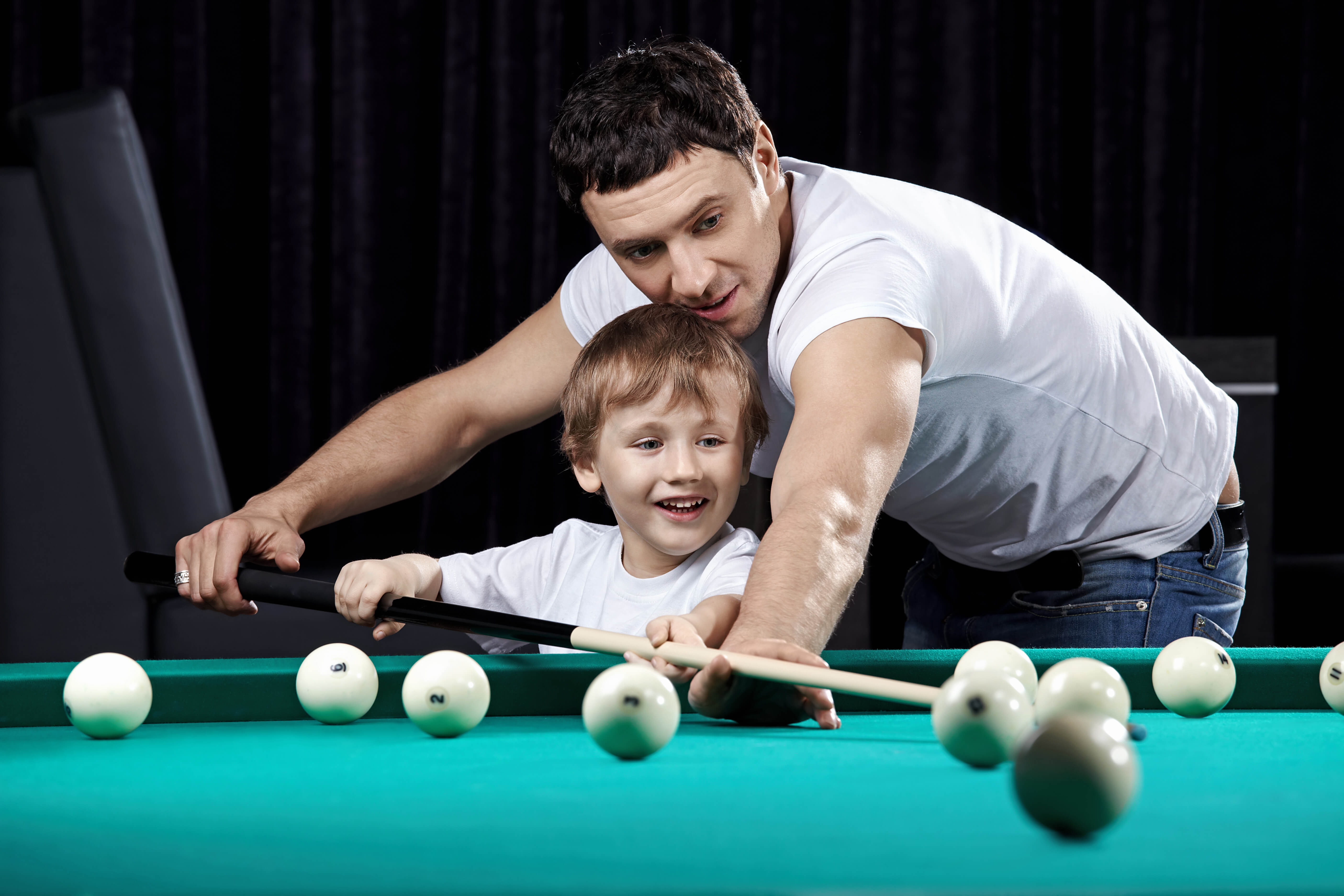 Father and son play pool billiards together