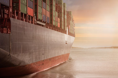 A freight ship sailing into a sunset.