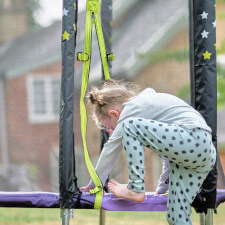 Kid playing on Plum Junior Stardust Springsafe trampoline with enclosure.