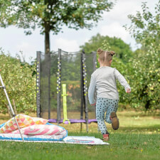 Kid playing Plum Junior Stardust Springsafe trampoline with enclosure.