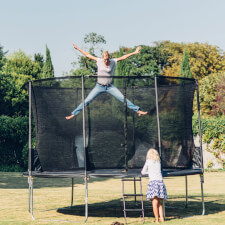 Adult bouncing on the Plum Space Zone II Springsafe trampoline with enclosure.