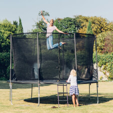 Adult bouncing on the Plum Space Zone II Springsafe trampoline with enclosure.