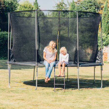 Adult and kid seatted on the Plum Space Zone II Springsafe trampoline with enclosure.